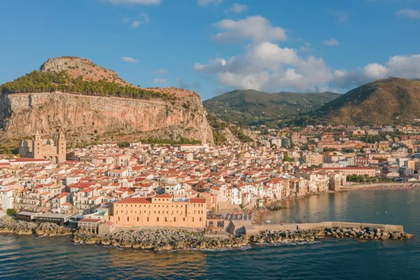 Vista panoramica di una città costiera con case dai tetti rossi ai piedi di una montagna.
