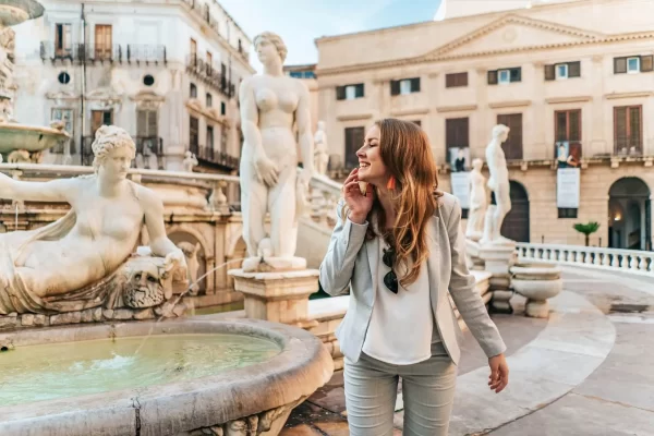 Donna sorridente in posa davanti alla Fontana Pretoria a Palermo, circondata da statue classiche.